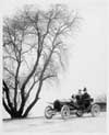 1907 Packard 30 Model U runabout with two passengers in winter by tree