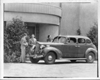 1938 Packard touring sedan parked in front of building, two men and woman by on right side of car