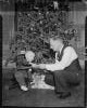 Boy on tricycle with elderly man by Christmas tree