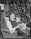 Elderly man reading to boy by Christmas tree