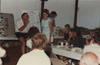 Award ceremony following the 5th Annual QWL (Quality of Work Life) Golf Outing.  Year unknown.  Subject seated on the table is John Rosendahl.  Woman standing is Judy Devers.  Other subjects unknown.  QWL began in the early 1980s.  It was an attempt by GM and the UAW to empower employees, improve communication, and improve morale.  Several activities like this golf outing were conducted under the umbrella of QWL.